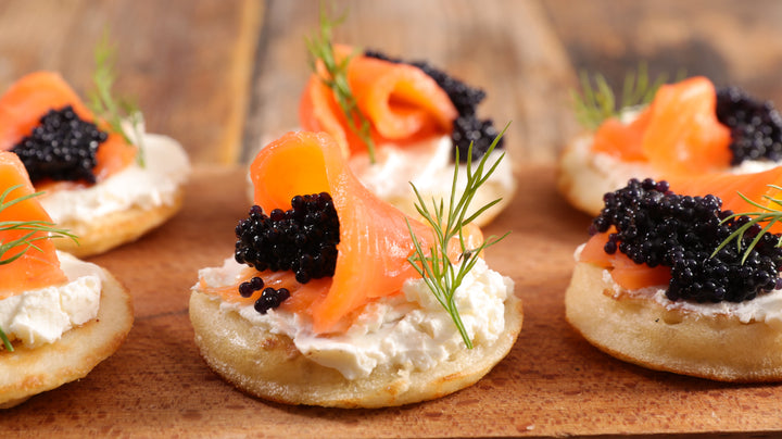 Kitchen countertop with several homemade Blini and Caviar sitting on top looking impressive.